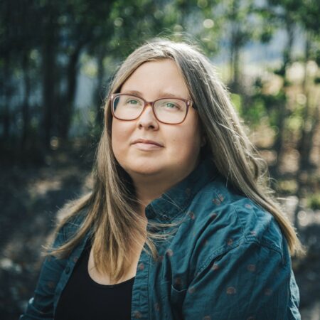 Jacq's headshot. They are wearing glasses and not looking at the camera.