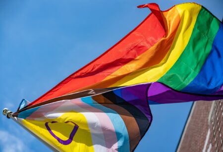 A Progress Pride flag blowing in the wind. Photo by Chris Robert on Unsplash.