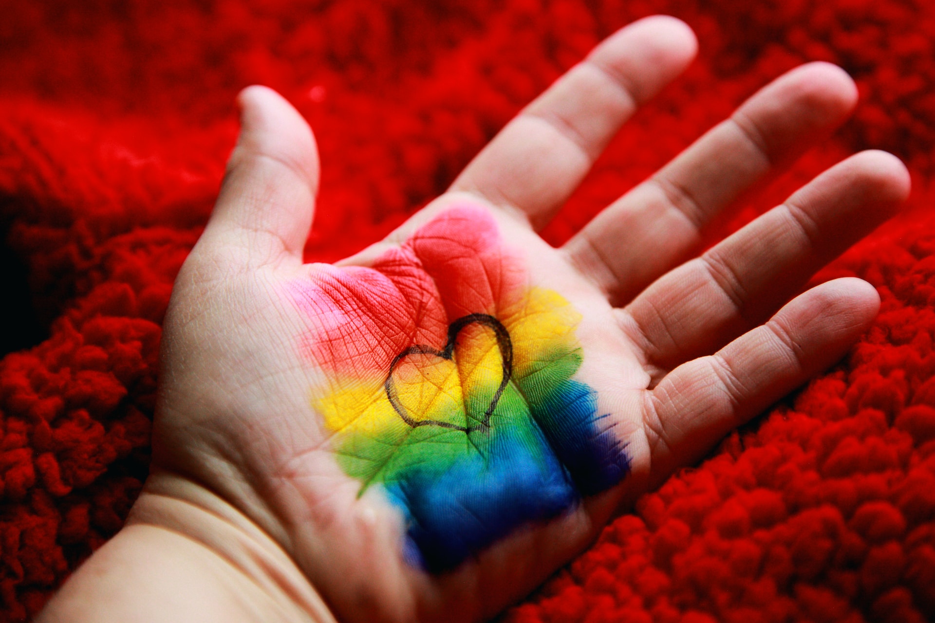An open hand with rainbow colours and a black heart in the middle