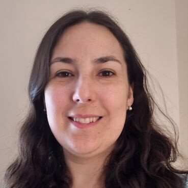 Angélique smiling against a neutral background. She has shoulder length dark, wavy hair. 
