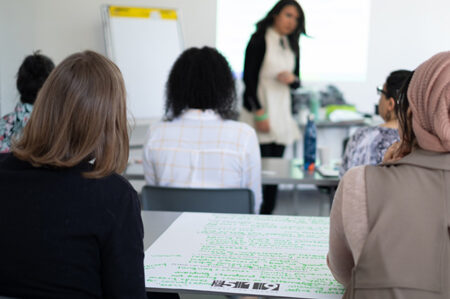 Two people sitting at a table in a classroom with a large sheet of paper between them.